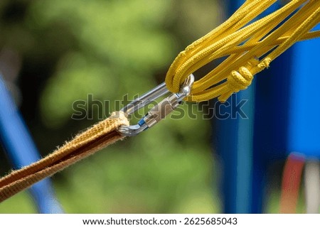 A yellow rope is connected to a metal object with a clasp. The rope is attached to a blue object