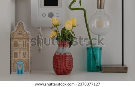 Yellow roses in Red ceramic vase, Lucky bamboo, Intercom handset - Door entry, Light bulb and tin music box. Home decor, Space for text, Selective focus.
