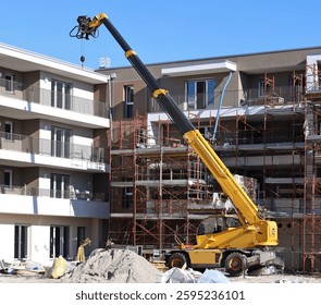 Yellow rotating telehandler at work in front of two new building under construction.
