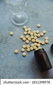 Yellow Round Tablets Or Pills Vitamins Flat Lay On Blue Stone Concrete Table With Black Plastic Bottle And Glass Drinking Cup, Top Down View, Vertical Stock Photo Image Still Life Background