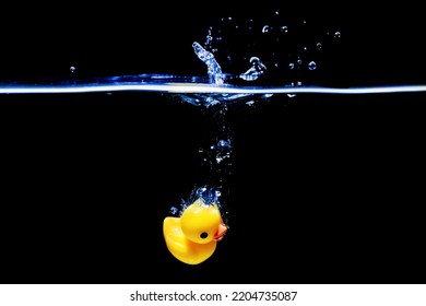 Yellow Rubber Duck Sinking Underwater In A Transparent Water Tank Isolated On Black Background.