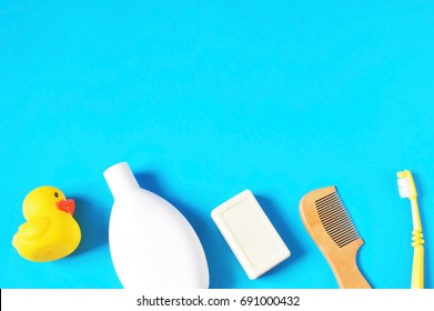 Yellow Rubber Duck, White Shampoo Bottle, Baby Soap, Wooden Comb And Toothbrush On A Blue Background. Flat Lay Bath Products, Top View