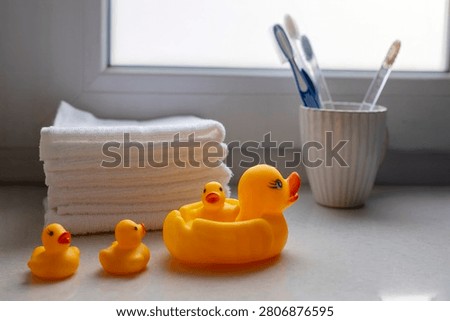 Yellow rubber ducks of different sizes beside folded white towels and toothbrushes in a cup on a bathroom counter
