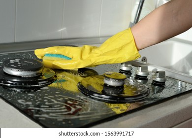 In a yellow rubber glove, a hand cleans a gas stove. Kitchen cleaning - Shutterstock ID 1563991717