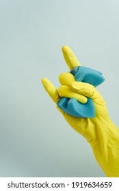 Yellow Rubber Glove Is Holding Sponge On The White Background. Yellow Rubber Glove Is Showing Rock Sign