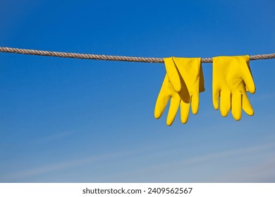 Yellow rubber protective gloves for work or cleaning hang on a rope and dry in the sun beams against a blue sky background - Powered by Shutterstock