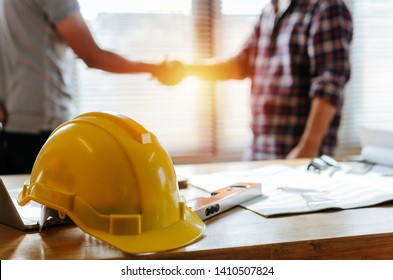 yellow safety helmet on workplace desk with construction worker team hands shaking greeting start up plan new project contract in office center at construction site, partnership and contractor concept - Shutterstock ID 1410507824