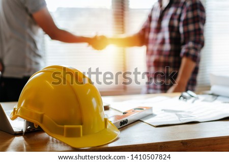 yellow safety helmet on workplace desk with construction worker team hands shaking greeting start up plan new project contract in office center at construction site, partnership and contractor concept Сток-фото © 
