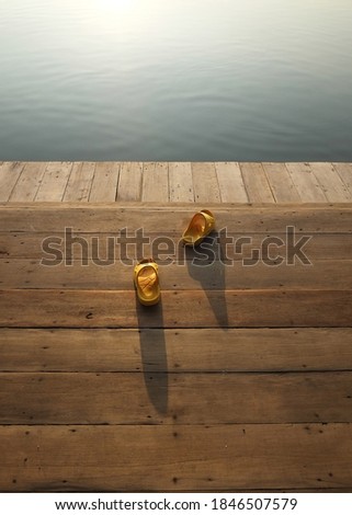 yellow scandals rubber shoes laid on the golden light brown wooden board of plank pier at river side port  in the sunset moment