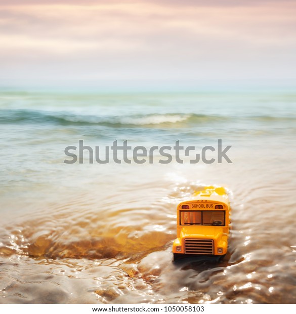 Yellow school bus ( toy model ) coming through the\
sea wave,morning beach.