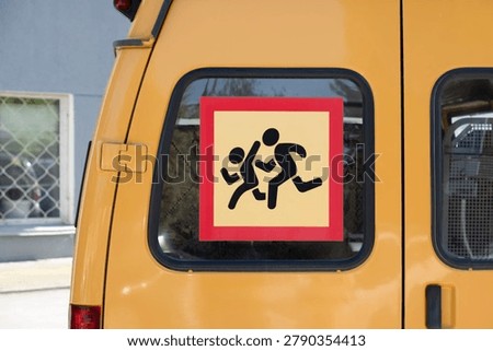 Yellow school bus window featuring a clear caution children warning sign sticker with running kids silhouette for child traffic safety and student transportation concept.