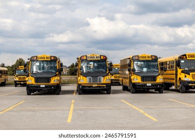 Yellow school buses lined up in an empty parking lot - under a partly cloudy sky. Taken in Toronto, Canada.