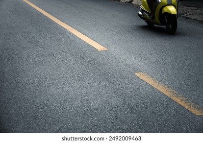 A yellow scooter is parked on the side of a road. The road is empty and the scooter is the only thing visible - Powered by Shutterstock