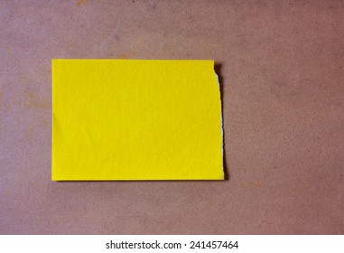 A Yellow Scrap Of Paper On A Brown Board