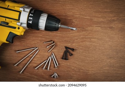 yellow screwdriver battery powered drill with screws of various sizes on wooden background.                                                  