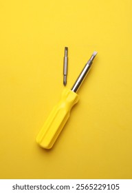 Yellow screwdriver with bits on yellow background
