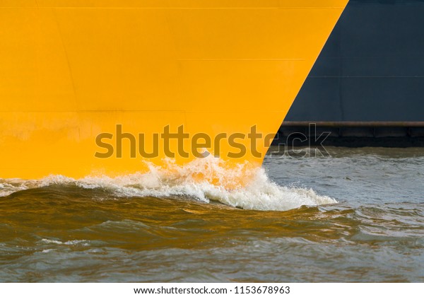 A yellow\
ship\'s bow in motion in the harbor.\
