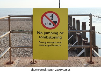 A yellow sign by the sea prohibiting jumping or tombstoning due to strong currents and submerged hazards - Shutterstock ID 2205992615