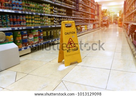 Yellow sign - caution. Wet floor is in the supermarket against the background of blurry products standing on the shelves