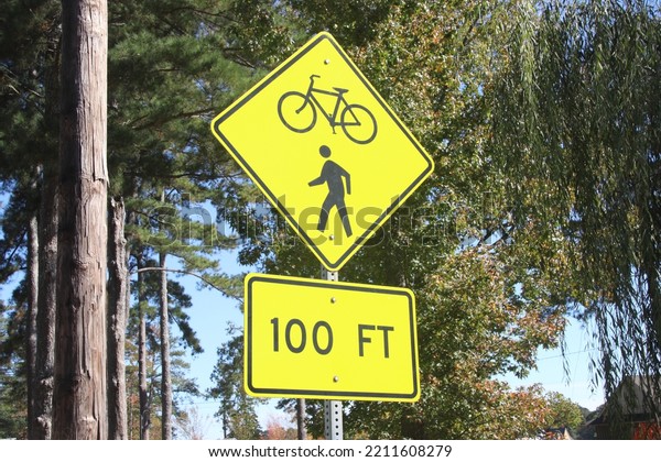A yellow sign indicating a bicycle and\
pedestrian crossing with trees in the\
background