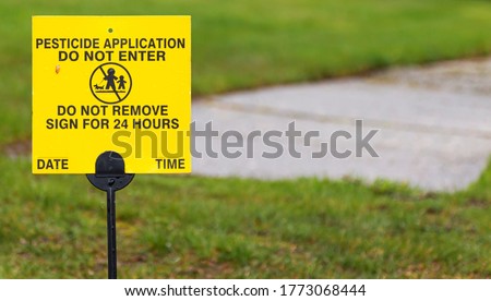 A yellow sign place on a residential lawn reads Pesticide applicatiion, do not enter for 24 hours.