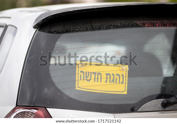 Yellow sign in the rear windshield of a vehicle\
in Hebrew for a female New Driver (for the editor: Hebrew - New\
female driver)