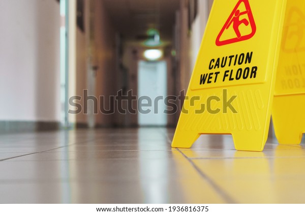 Yellow\
sign of slippery floor in the room after cleaning. A sign that\
reads Caution is a long empty industrial\
corridor.