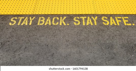 Yellow Sign At Train Station Asking People To Stay Back, Stay Safe, On Concrete Floor