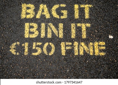 Yellow Sing On A Dark Asphalt To Dog Owners To Clean Up Dog Poo. Bag It, Bin It. 150 Euro Fine.