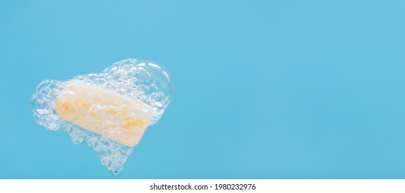 Yellow soap surrounded by soap bubbles and heart-shaped foam on a blue background. The joy and love of body care procedures. Copy space. Banner - Powered by Shutterstock