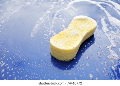 Yellow Soapy Sponge On The Hood Of A Blue Car.