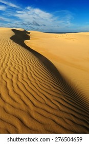 Yellow Soft Sand Dunes In Desert With Sand Patterns And Lines And Shadows With Distant Water Or Mirage