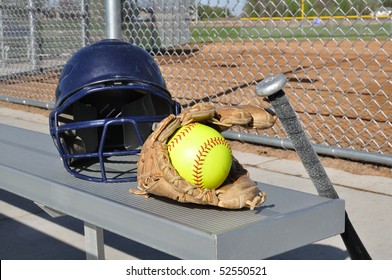 Yellow Softball, Helmet, Bat, And Glove On An Aluminum Bench