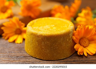 Yellow solid shampoo bar and flowers on wooden table, closeup. Hair care