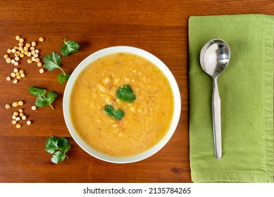 Yellow Split Peas Lentil Soup, Garnished With Corrinader Leaves, In A Bowl With A Spoon And Napkin On A Wooden Table. View From Above.