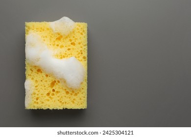 Yellow sponge with foam on grey background, top view. Space for text