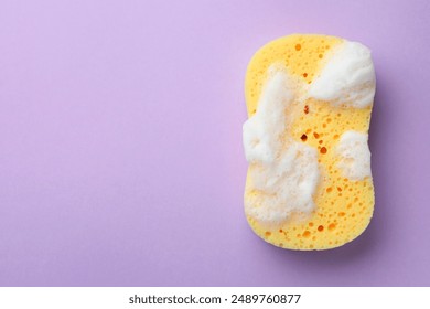 Yellow sponge with foam on violet background, top view. Space for text