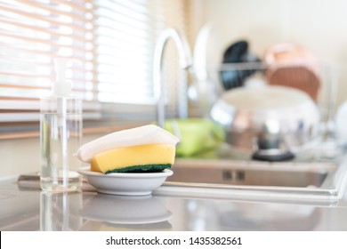 Yellow Sponges And Dish Washing Liquid Soap On Dirty Sink Fully With Dishes And Kitchen Ware.