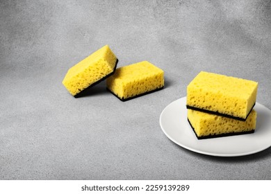Yellow sponges for dishwashing on a white plate on a neutral gray background. Gentle dishwashing. House cleaning - Shutterstock ID 2259139289