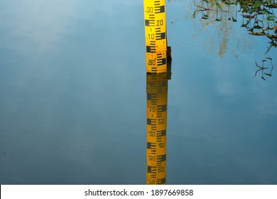 Yellow Staff For Water Level Measurement Reflected On The Surface Of Still Water