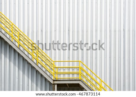 The yellow stair for fire escape with the steel wall of the factory building.The factory wall building and the yellow stair building 
