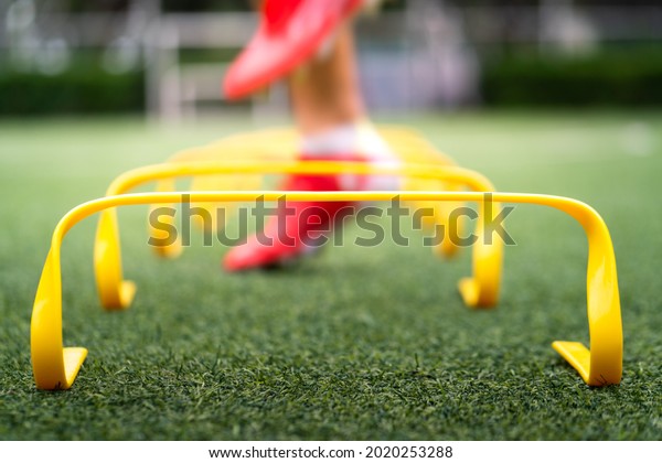 A yellow step-over ladder for speed and leg\
strength training equipment (Focus), Photo with action of a sport\
player is training on it as blurred background. Sport object and\
action photo.