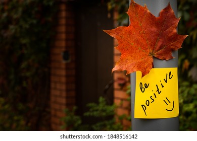 gelber Aufkleber mit den Worten positiv und rotes Herbstblattblatt auf einer grauen Betonsäule auf rotem Zaun und einem Tor