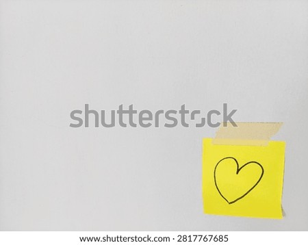 Yellow sticky note featuring hand drawn heart symbol taped to wall background with copy space, for love, Valentine's Day, anniversary, affection, relationship, romance, and romantic message concepts.