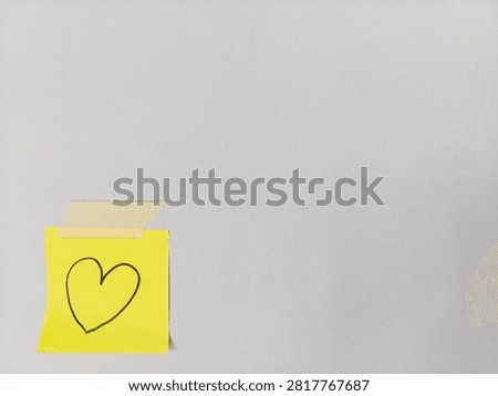Yellow sticky note featuring hand drawn heart symbol taped to wall background with copy space, for love, Valentine's Day, anniversary, affection, relationship, romance, and romantic message concepts.