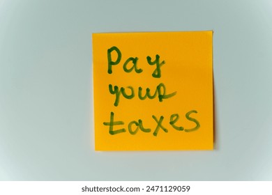 A yellow sticky note with the handwritten message Pay Your Taxes