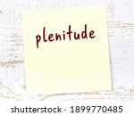 Yellow sticky note on wooden wall with handwritten inscription plenitude