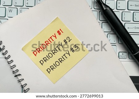 Yellow sticky note with Priority #1, #2, and #3 on office desk with keyboard and notebook. Concept of task prioritization, time management, productivity, and business planning.