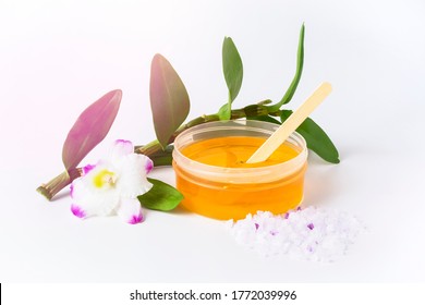 Yellow sticky sugaring wax paste for hair removing with wooden spatula stick, violet orchid flower and peeling sea salt. Light background and lightleak flare