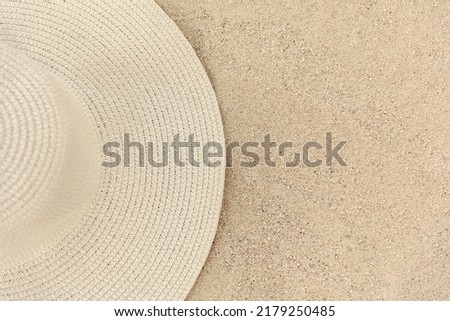 Yellow straw women's hat lies on the sand, top view, half of the hat